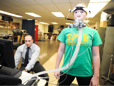 A researcher on a computer and a woman with respiration monitoring equipment on her face.